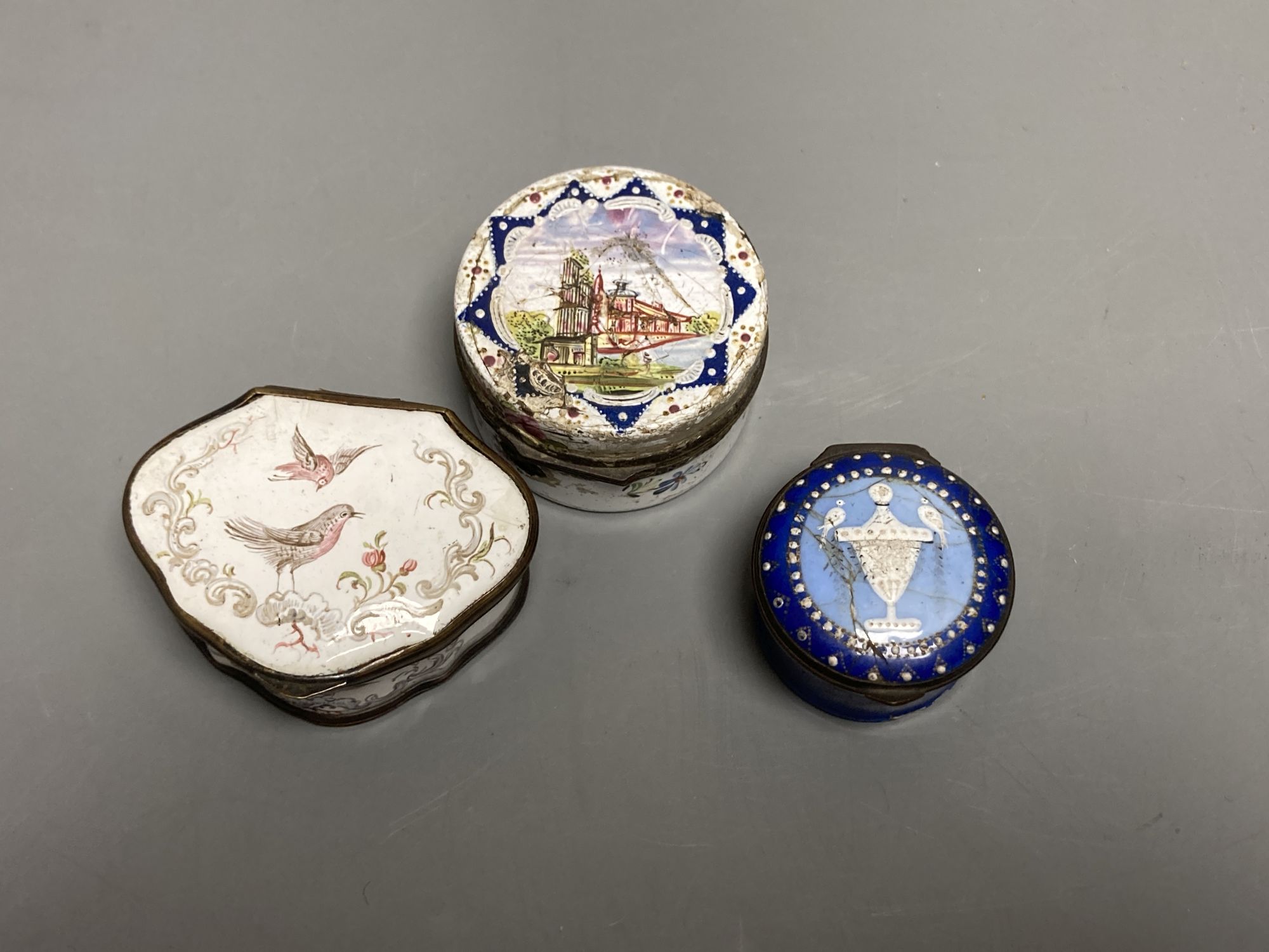 An 18th century white enamelled box painted with a palace, 5cm., a cartouche shaped box decorated with a birds, 6cm. and a patch box de